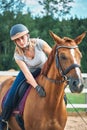 Girl rider in helmet stroking horse sitting astride