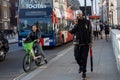 a girl rides a city bike in front of the bus. A man walks along the sidewalk, talking on the phone