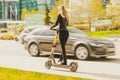 girl rides a kick scooter around the city along the road. Rear view of woman in black casual clothes riding electric scooter