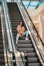 girl rides while sitting on the escalator. shopping mall, pretty brunette in a sporty style.