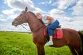 Girl riding on a horse on a green field and a blue sky with white clouds on the background Royalty Free Stock Photo