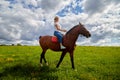 Girl riding on a horse on a green field and a blue sky with white clouds on the background Royalty Free Stock Photo