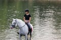 Girl riding a snow white horse down the calm river water Royalty Free Stock Photo