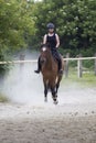 The girl is riding sorrel horse on a dusty track