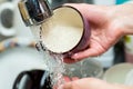 Girl rinses a cup under running water in the kitchen, closeup