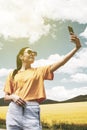 Girl on the road, in a yellow T-shirt, taking a photo in a flowering field, against the backdrop of mountains