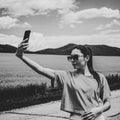 Girl on the road, in a yellow T-shirt, taking a photo in a flowering field, against the backdrop of mountains