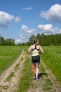 Girl runs along a road that runs through fields under a blue cloudy sky on a summer day. Royalty Free Stock Photo