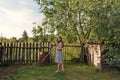 A girl in a rustic old-fashioned dress goes holding a rake over a rural garden courtyard