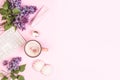 Girl`s desktop. A bouquet of lilacs, a keyboard, a cup of coffee, cakes, face cream on a pink background.