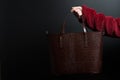 Girl`s hand holds brown leather bag on black background, bag in female hand side view on black background, leather handbag holds f