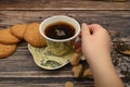 The girl`s hand holds a mug of black tea, oatmeal cookies, tea leaves, brown sugar on a wooden background. Close up Royalty Free Stock Photo