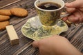 The girl`s hand holds a mug of black tea, oatmeal cookies, waffles, tea leaves, brown sugar on a wooden background. Close up Royalty Free Stock Photo