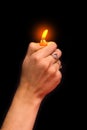 The girl's hand lights the bright fire of the lighter, the light in the darkness on a black background