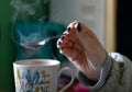 Girl's hand with a spoon over a mug with steam curling up