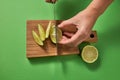 A girl`s hands cut a green natural lime to slices with sharp knife on a wooden board on a green. Top view. Royalty Free Stock Photo