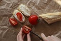 The girl`s hands are cutting a tomato on a brown background, next to it lies a sliced baguette, a fresh tomato and two sandwiches Royalty Free Stock Photo