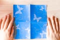 Girl`s hands making origami blue dress from butterfly printed paper. Step by step instruction, step 3. Mother`s day, birhday,