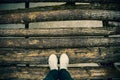 The girl`s legs in blue jeans and silver shoes with white laces stand on a old wooden log bridge over the river. Old village Royalty Free Stock Photo