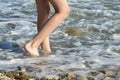 The girl`s legs go into the sea surf on a pebble beach in the sun. The concept of tourism Royalty Free Stock Photo