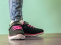 The girl`s legs in torn jeans and black and red sneakers on the brown wooden floor near the blue wall. Royalty Free Stock Photo