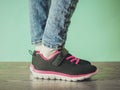 The girl`s legs in torn jeans and black and red sneakers on the brown wooden floor near the blue wall. Toned. Royalty Free Stock Photo