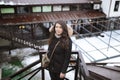 The girl`s portrait in a black short fur coat who stands behind a handrail and looks in a distance in the winter