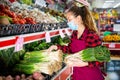 Girl salesperson in a protective mask puts leeks on a display case