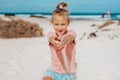 Girl with sand falling from his clnched fist, standing on beach. Family summer vacation by sea. Royalty Free Stock Photo