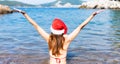 Girl in santa hat and in a bikini holding her hands up stands on the beach by the sea. Back view. Concept for Christmas and New Royalty Free Stock Photo