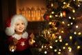 A girl in a Santa hat decorates the Christmas tree on Christmas eve and smiles sweetly in anticipation of the holiday