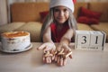 Girl in Santa hat shows burnt candles of numbers of outgoing year in her palms, festive background
