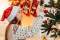 Girl in Santa hat smiling and hanging multi-coloured balls on Christmas tree Royalty Free Stock Photo