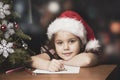 Girl in Santa hat writes gift list. Vintage style Christmas child portrait Royalty Free Stock Photo