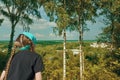 A girl in a scarf looks from a glance or hill at the landscape of nature, white birches stand in ripples, part of the roofs from Royalty Free Stock Photo