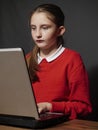 Girl in school red uniform working on a notebook, looking at the screen, hands on keyboard. Concept modern technology used by