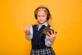 A girl in a school uniform with headphones on her head holds a smartphone in her hands and shows a gesture of victory Royalty Free Stock Photo