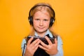 Girl in a school uniform with headphones on her head listens to music and holds a smartphone in her hands Royalty Free Stock Photo