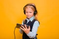 Girl in a school uniform with headphones on her head listens to music and holds a smartphone in her hands Royalty Free Stock Photo