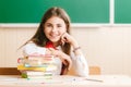 Girl in school uniform sitting at her desk in the classroom with books. Student in class at school