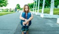 Girl schoolgirl 12-15 years old, sitting in the summer in the city on a skateboard, asphalt road. Sad tired, rest after Royalty Free Stock Photo