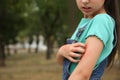 Girl scratching arm with insect bites in park, closeup. Space for text