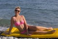 Girl at the sea. Attractive blonde-haired woman sunbathes recline on inflatable swimming mattress on pebble beach Royalty Free Stock Photo