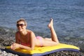 Girl at the sea. Attractive blonde-haired woman sunbathes recline on inflatable swimming mattress on pebble beach Royalty Free Stock Photo