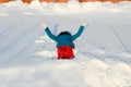 A girl in a sea-green color jacket and orange bolognese sports pants is lying on white freshly fallen deep snow and waving her
