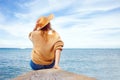 Girl at the sea looks at the horizon, woman in a sun hat sits on the pier in summer and dreams, vacation concept