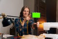 A girl seamstress keeps a blog about sewing in a workshop at home. Craftsman holds smartphone with green screen