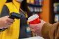 girl seller holds a barcode scanner in her hands and is counting on a man with a glass of coffee in his hand