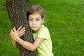 Girl with serious face stands, embracing tree