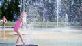 A girl of seven years, in swimsuit, bathe in the fountain, run around, squirt, have fun, on a hot summer day. Slow